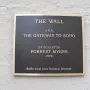 A dark metallic plaque for The Wall mounted on a light textured wall.