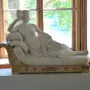 Reclining white marble statue of Venus Victrix on an ornate chaise lounge in a gallery room