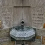 Stone holy water font at the National Shrine of the Little Flower with a metal spigot and carved inscription.