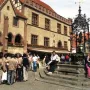 Gänseliesel Fountain in a town square, with a statue beneath an ornate dark spire and people sitting on the steps.