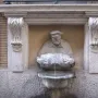 The Porter fountain statue, shown as a small figure carrying a barrel over his shoulder beside a building.