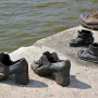 Metal shoes from the Shoes on the Danube Bank memorial on a concrete riverbank with calm water behind them.