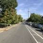 Trenton Battle Monument rises in the distance beside an American flag along a tree-lined street.