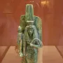 Ancient Egyptian statue of Queen Tiye with a tall headdress and patterned garment, holding a fan-like object.