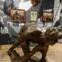 Bronze sculpture of a muscular man bent over gripping a large stone, displayed on a pedestal in a museum.