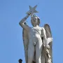 Weathered marble figure atop the Genio Catalán Fountain, holding a star overhead with pigeons perched on the base and shoulder.