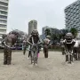 A-maze-ing Laughter statues standing on sandy ground with city buildings and trees behind them.