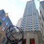 Atlas sculpture showing a kneeling muscular man holding up an armillary sphere in front of skyscrapers.
