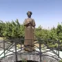 Bronze statue of Zabel Yessayan holding a book, standing on an arched bridge with roses and trees behind her.