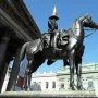 Duke of Wellington bronze equestrian statue with a traffic cone on the rider’s hat, set against a grand building under a blue sky.