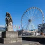 Tauzieher statue of a man securing a thick rope around a bollard, with a Ferris wheel and waterfront buildings in the background.