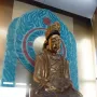 A gilded seated statue with a crown and ornate robes displayed against a carved blue and red backdrop at Huangze Monastery Rock Sculptures.