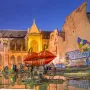 Stravinsky Fountain with colorful abstract sculptures, including red lips and a bird-like figure, beside an illuminated Gothic building at dusk.