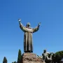 Bronze Monument to Saint Francis of Assisi with robed figures on a stepped stone plinth under a blue sky.