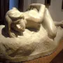 Malgré Tout sculpture of a reclining nude woman on a museum display stand