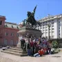 Manuel Belgrano equestrian statue on a tall pedestal in a city square, with people gathered around the base.