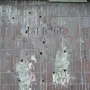 Worn Plon relief wall with reddish-brown vertical tiles, missing patches, and white residue