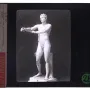 Classical Apoxyomenos statue of a nude male athlete extending his arms in a scraping pose against a dark background.