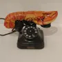 Lobster Telephone sculpture combining a black rotary phone with a bright red-orange lobster on the receiver cradle.