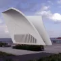 Postcards 9/11 Memorial with two white curved structures on a waterfront promenade, with a ferry and city skyline in the background.