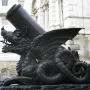 The Cádiz Memorial shows a large mortar mounted on a dark dragon-like sculpture, with a white building and equestrian statue in the background.