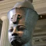 Colossal granite head of Amenhotep III displayed on a white pedestal in a museum