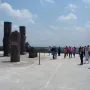 Tall stone Atlantean Figures at Tula standing on a wide plaza with tourists and a bright blue sky overhead.