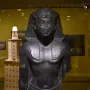 Upper portion of a Ptolemaic King statue with a headdress, damaged nose, and missing arms.