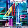 Big 4 sculpture in bright colours stands in front of a modern glass-and-steel building.