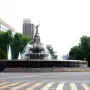 Diana the Huntress Fountain with a tall statue and water spraying from a multi-tiered stone base at a city intersection.