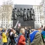 The Monument to the Women of World War II stands behind a crowd of protesters in a city square.