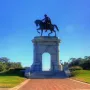 Sam Houston Statue on a stone archway with a rider on horseback above a grassy knoll and brick walkway.