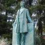 Lincoln the Lawyer bronze statue of Abraham Lincoln standing outdoors on a pedestal with evergreen trees behind it.