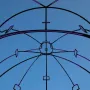 Memoria Urbana’s black metal framework lit with purple lights against a blue sky.