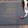 Dark grey plaque on the Monument of Gratitude to the Iranian People with gold Polish and Persian inscriptions and a white-and-red ribbon draped over one side.