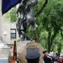Buckey O\'Neill Monument, an equestrian bronze statue on a rock base, with uniformed people gathered below and a ceremonial flag in front.