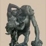 Gorilla Carries a Woman sculpture showing a gorilla standing upright with a woman slung over its shoulder, holding a rock on a rocky base.