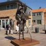 Survival of the Fattest bronze sculpture showing a large woman carrying scales and a staff on the shoulders of an emaciated figure.