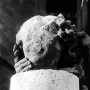 Damaged stone head of the Smiling Angel with a faint smile, held by two hands above a stone pedestal.