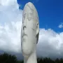 The Dream sculpture by Jaume Plensa, a tall white head and neck with closed eyes, against a blue sky with clouds.