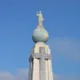 Divino Salvador del Mundo monument showing a robed figure raising one arm atop a globe and stone pedestal against a blue sky.