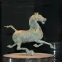 Weathered bronze Flying Horse of Gansu sculpture in a galloping pose on a pedestal inside a display case.