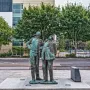 Two Working Men sculpture showing two weathered bronze figures standing side by side on a stone plinth, both looking upward to the left.