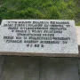 Granite memorial plaque for the Monument of Common Martyrdom with raised Polish lettering and two white candles beside it.