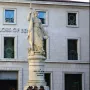 Monumento dell\'Indipendenza, a stone female statue holding a sword and wreath atop a tall pedestal with people seated on the steps below.
