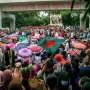 Anti Terrorism Raju Memorial Sculpture beside a large crowd with umbrellas, Bangladeshi flags, and a concrete archway in the background.