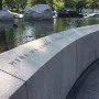 Curved stone wall of the Japanese American Memorial inscribed with “HERE WE ADMIT A WRONG,” beside a reflecting pool and boulders.