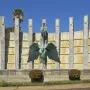 Monumento a Franco with a bronze robed figure holding a sword atop a winged figure in front of a curved stone wall and pillars.
