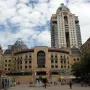 Nelson Mandela statue with raised arms in a busy public square, standing behind a fountain.