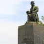 Bronze monument of Vuk Karadžić seated on a tall stone pedestal, holding a book, with trees and a cloudy sky behind it.
